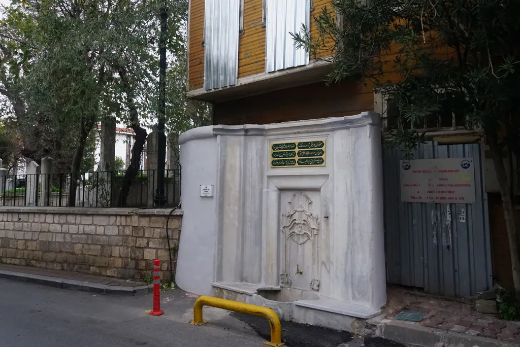 Nişancı Mehmed Paşa Camii'nin karşısında Ebubekir Ağa Çeşmesi; beyaz mermer cephe, yaldızlı kitabe levhası, kabartmalı ayna taşı ve sokak.