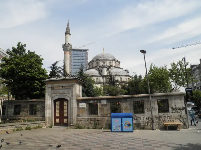 Şişli Meydanı'nda Şişli Camii; taş avlu duvarı ve ahşap kanatlı kapı, arkada kurşun kaplı kubbeler, ince minare ve bir gökdelen.