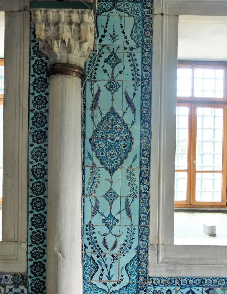 Çini kaplı bir paye ile yanındaki pencere; firuze ve lacivert bitkisel desenler, mermer sütun ve ahşap doğrama.