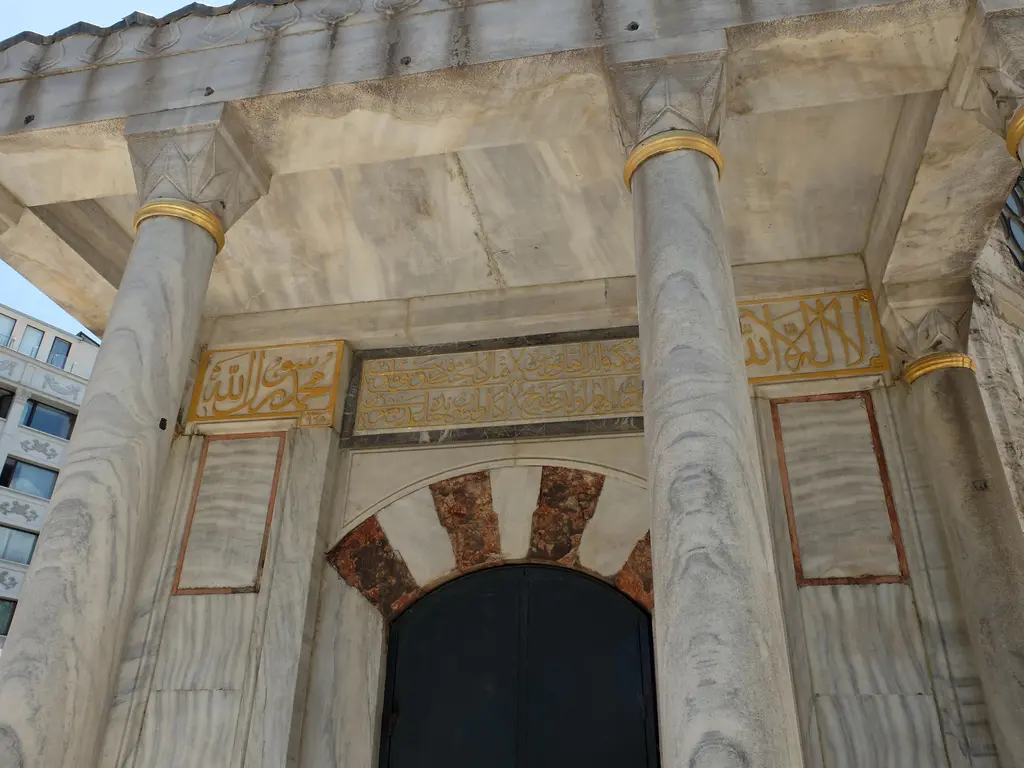 Şehzade Külliyesi'nde Rüstem Paşa Türbesi'nin revağı; yaldızlı başlıklı mermer sütunlar, kırmızı beyaz almaşık kemerli kapı ve üstünde yaldızlı kitabe panoları.