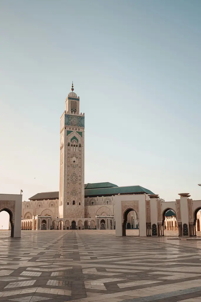 Fas'ta Kazablanka'daki II. Hasan Camii; çini işlemeli yüksek minare, geniş taş avlu ve kemerli revaklar, akşama doğru yumuşak ışık.