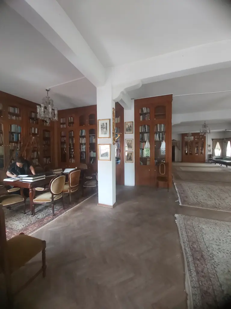 İstanbul Kitaplığı'nın okuma salonu; ahşap kitap dolapları, ortada beyaz bir sütun, avize, masa başında çalışan biri ve halılar.