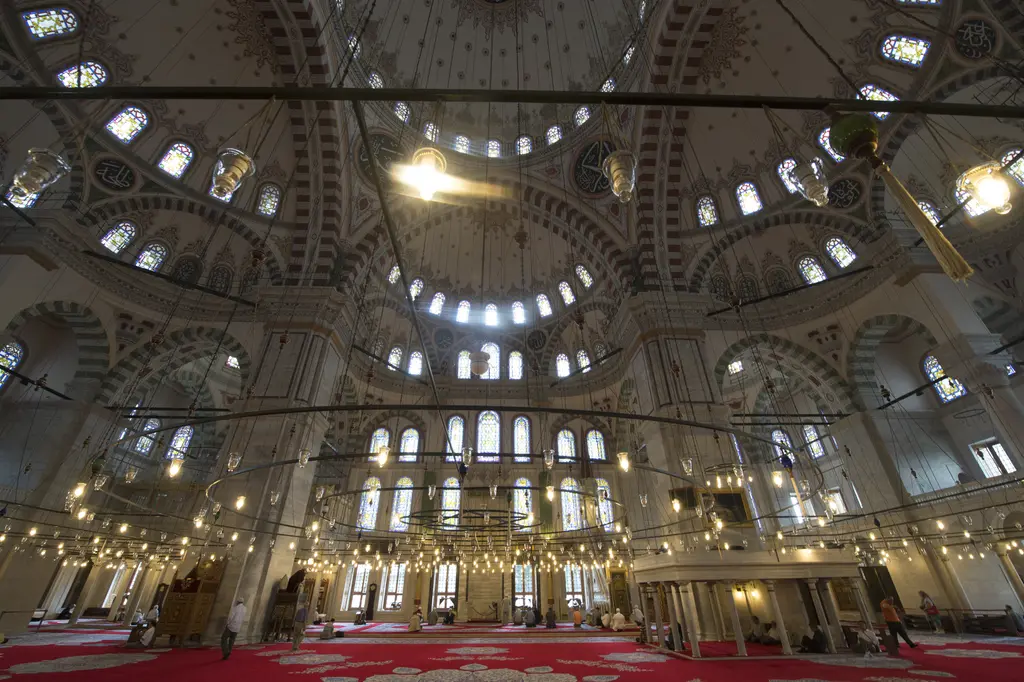 Fatih Camii'nde kubbe kuşağına geniş açıyla bakış; ana kubbe ile yarım kubbeler, yeşil ve kiremit renkli boyalı bantlar, altın hat madalyonları ve vitraylı pencere sıraları.