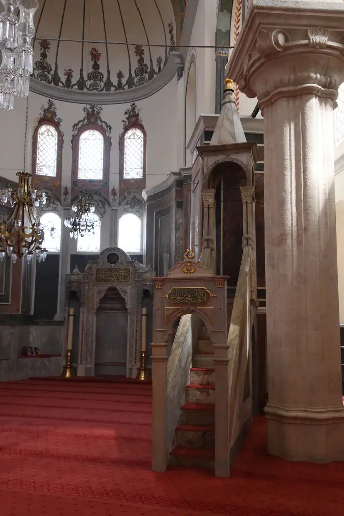 Zeyrek Camii'nin içinden bir görünüm; kırmızı halı, kalem işi bezeli kemerler, mermer kaplı duvar altlığı, pirinç avize ve geride mermer minberin gövdesi.