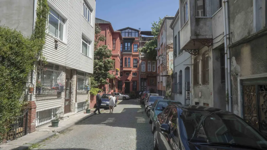 Kuzguncuk'ta parke taşlı Tahtalı Bostan Sokağı; sarmaşıklı ahşap ev, kırmızı cepheli binalar ve park etmiş arabalar.