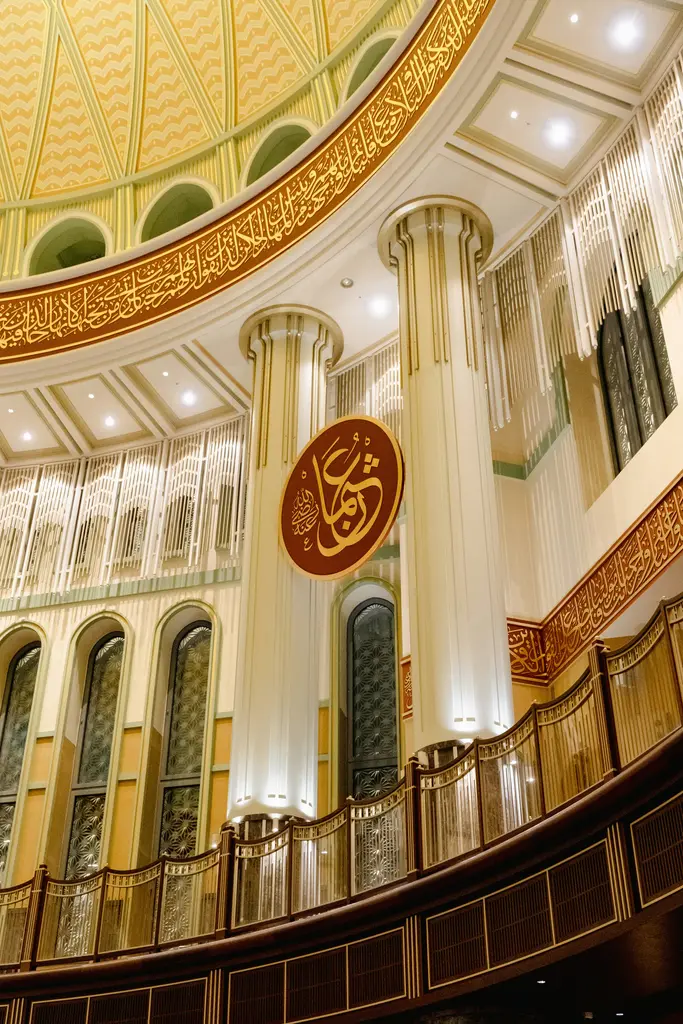 Taksim Camii'nin iç mekânı; altın yaldızlı kubbe kasnağı, beyaz sütunlar, kırmızı zeminli hat levhası ve ahşap korkuluklu kadınlar mahfili.