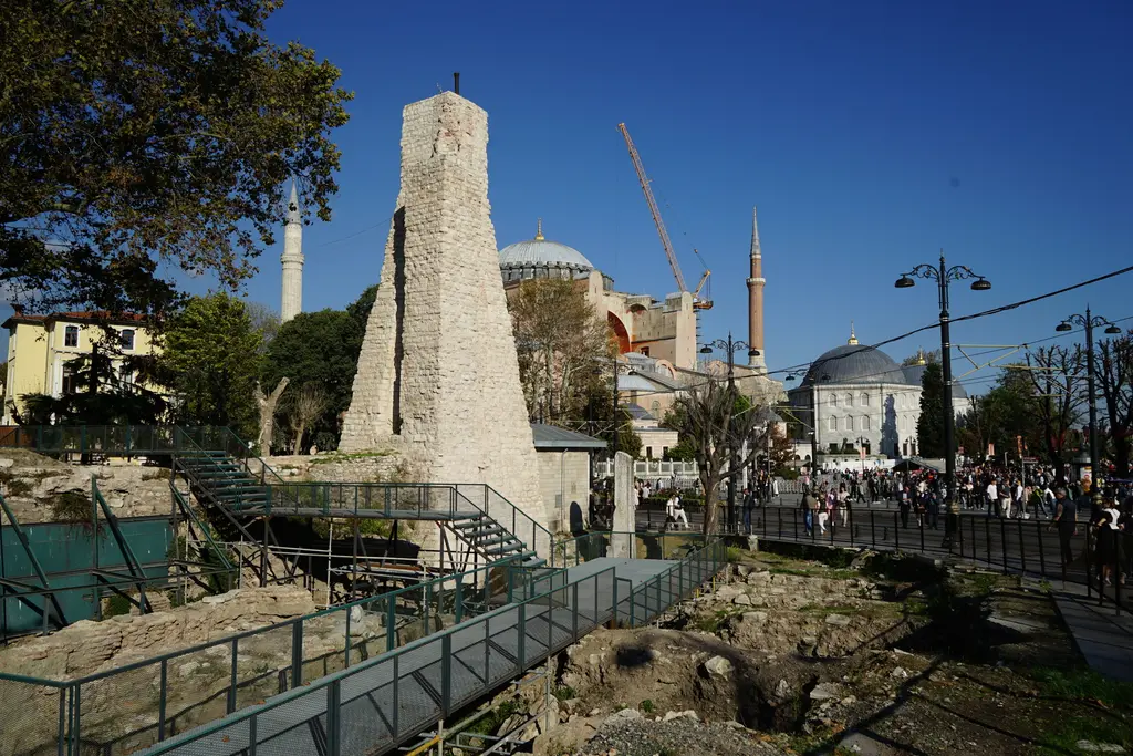 Sultanahmet'te Osmanlı su terazisi; çevresinde çelik yürüme yollarıyla kazı alanı, arkada Ayasofya'nın kubbesi, minareleri ve açık mavi gök.
