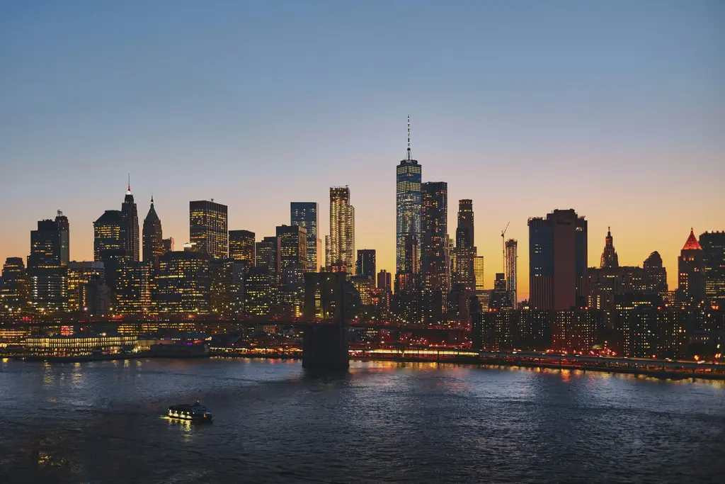 New York'ta Manhattan siluetinin gün batımında görünümü; Brooklyn Köprüsü ve One World Trade Center'ın ışıkları East River'ın sularına yansıyor.