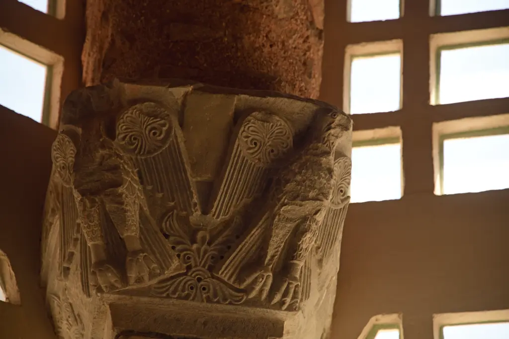 Fenari İsa Camii'nde devşirme mermer sütun başlığı yakın planda; derin oyulmuş palmet ile akant yaprakları, aşınmış krem mermer ve arkada şebekeli pencere.