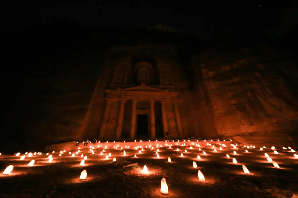 Gece karanlığında Petra'daki Hazine cephesi; önündeki kumlu meydanı boydan boya dolduran yüzlerce kâğıt fenerin turuncu alevleri ve loş biçimde aydınlanan kaya cephesi.