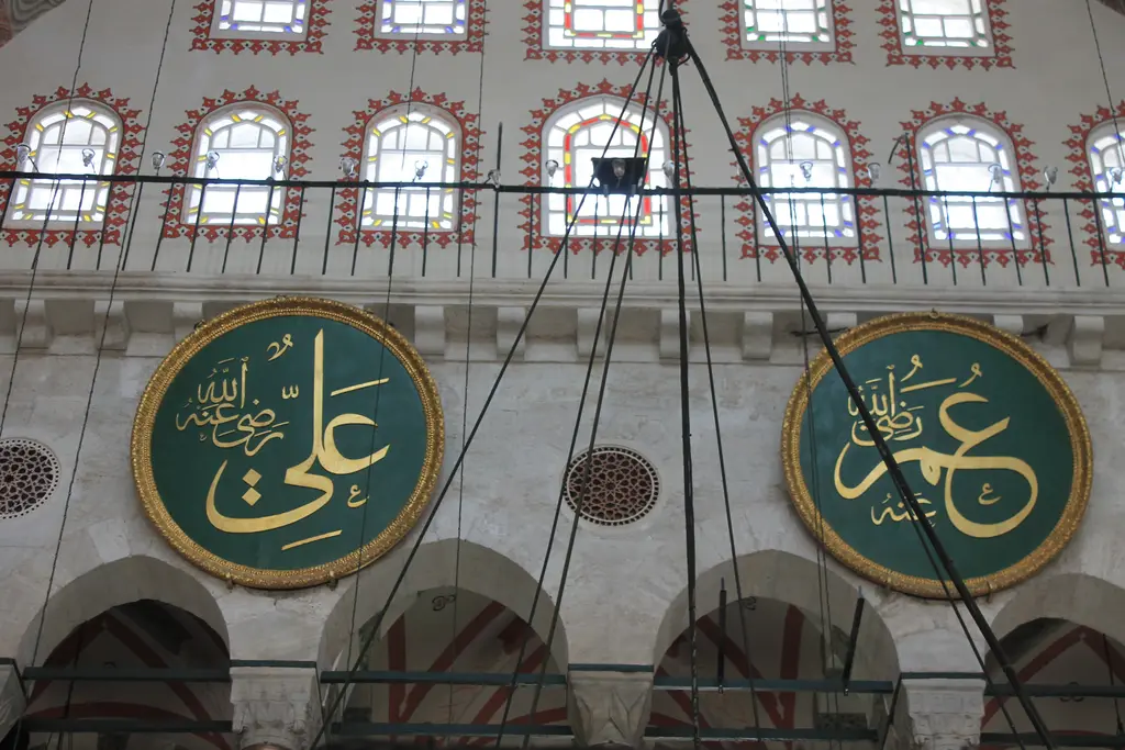Kılıç Ali Paşa Camii'nde galeri katı; sıra sıra kemerli pencereler, avize zincirleri ve yeşil zeminli iki büyük yuvarlak hat levhası.