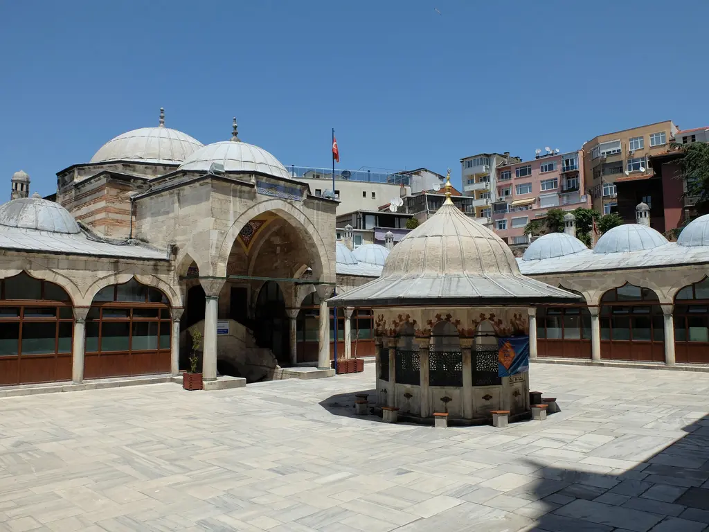 Sokullu Mehmed Paşa Camii'nin avlusu; ortada konik çatılı şadırvan, çevresinde revaklar, arkada kubbeler ve taş döşeli geniş zemin.