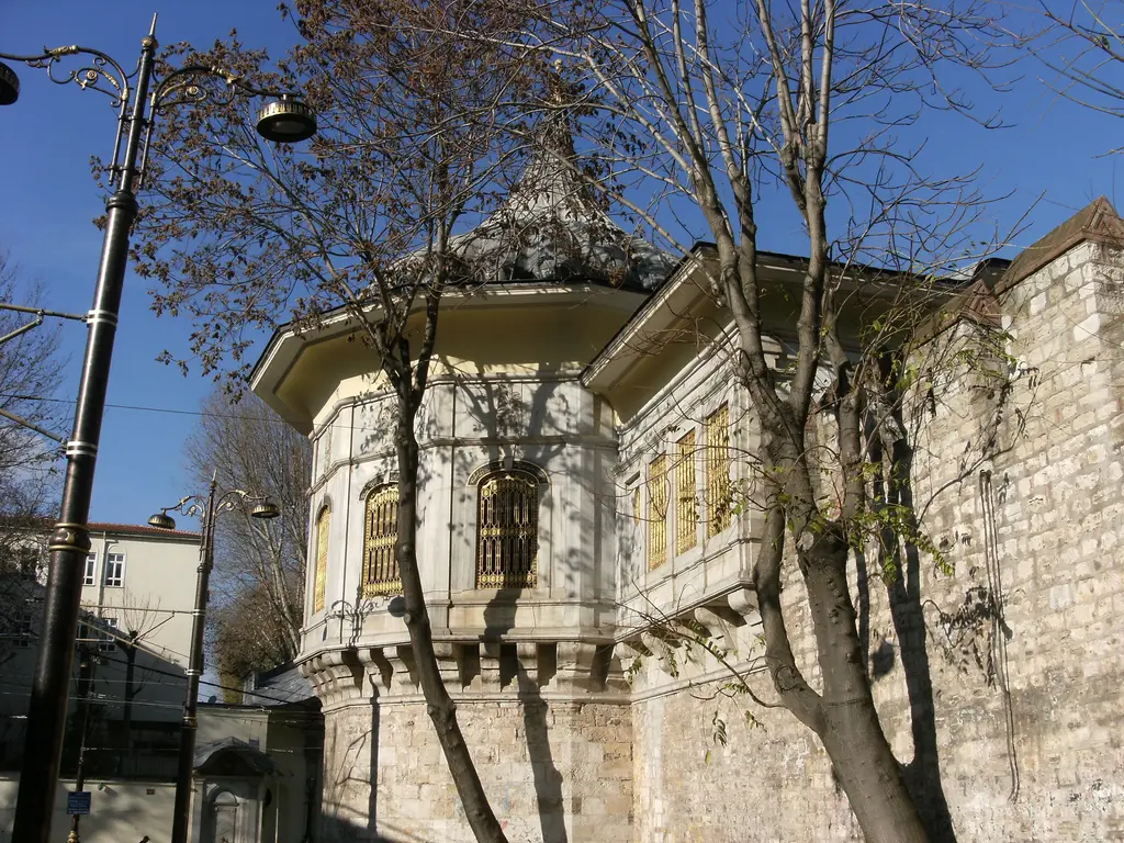 Yapraksız çınar dalları arasında Alay Köşkü; mermer salon, kafesli pencereler, sur boyunca uzanan kanat, sokak lambası ve mavi gök.