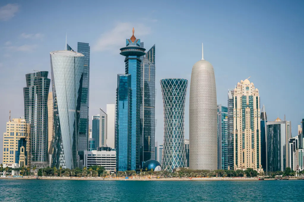 Doha'da West Bay silueti; deniz üzerinden görülen cam kaplı gökdelen kümesi, aralarında yükselen ince kuleler ve önde turkuaz körfez suyu.