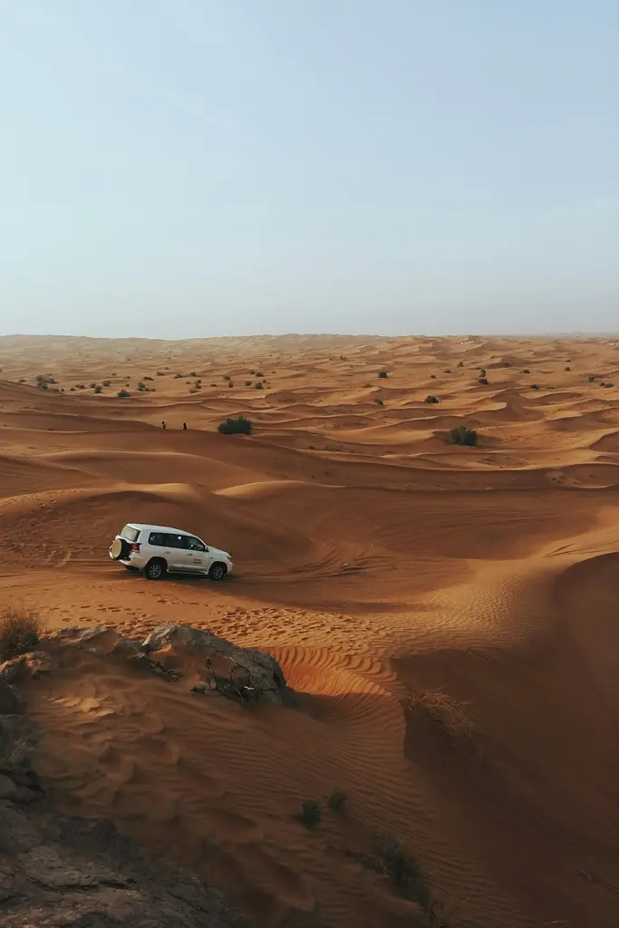Dubai yakınında çöl safarisi; turuncu kumulların üzerindeki arazi aracı ve uzanan kum dalgaları.