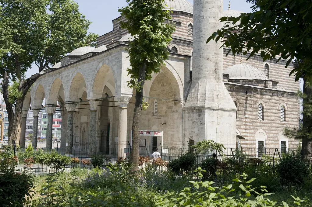 Murat Paşa Camii'nin son cemaat yeri; sivri kemerli revak, sütunlar, arkada kubbeler, köşede minare kaidesi ve önde yeşillik.