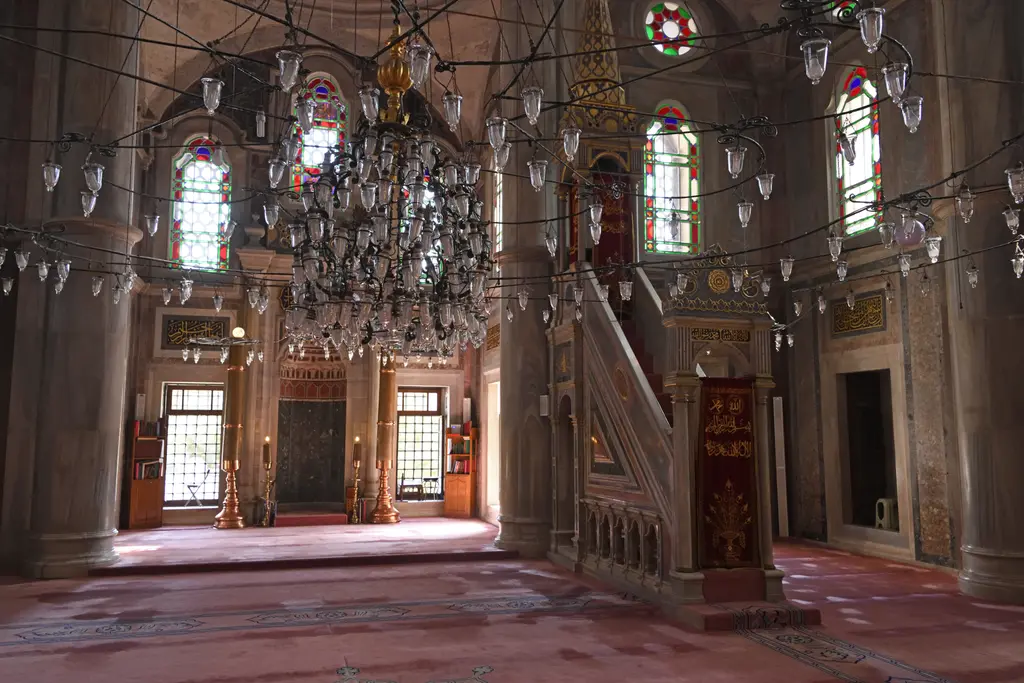 Laleli Camii'nde mihrap ve minber; sağda mermer minberin merdiveni ile külahı, solda mihrap, üstte avizeler ve renkli camlı pencereler.