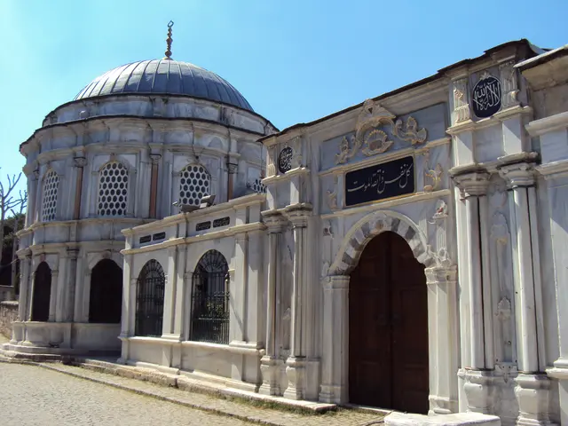 Eyüpsultan'da Mihrişah Valide Sultan Külliyesi; kurşun kubbeli beyaz mermer türbe, yaldızlı kitabeli sokak cephesi, ahşap kapı ve kafesli pencereler.