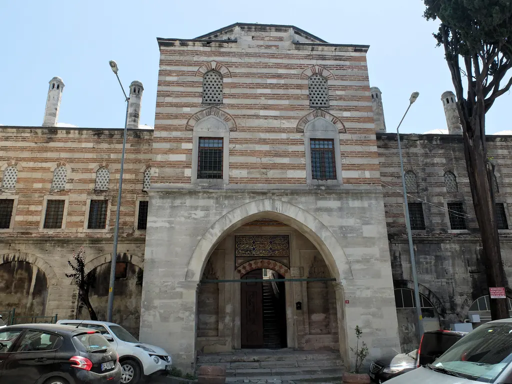 Sokullu Mehmed Paşa Camii'nin sokak cephesi; kesme taş duvar, sivri kemerli yüksek kapı, iki yanda pencereler ve kaldırımda park etmiş araçlar.