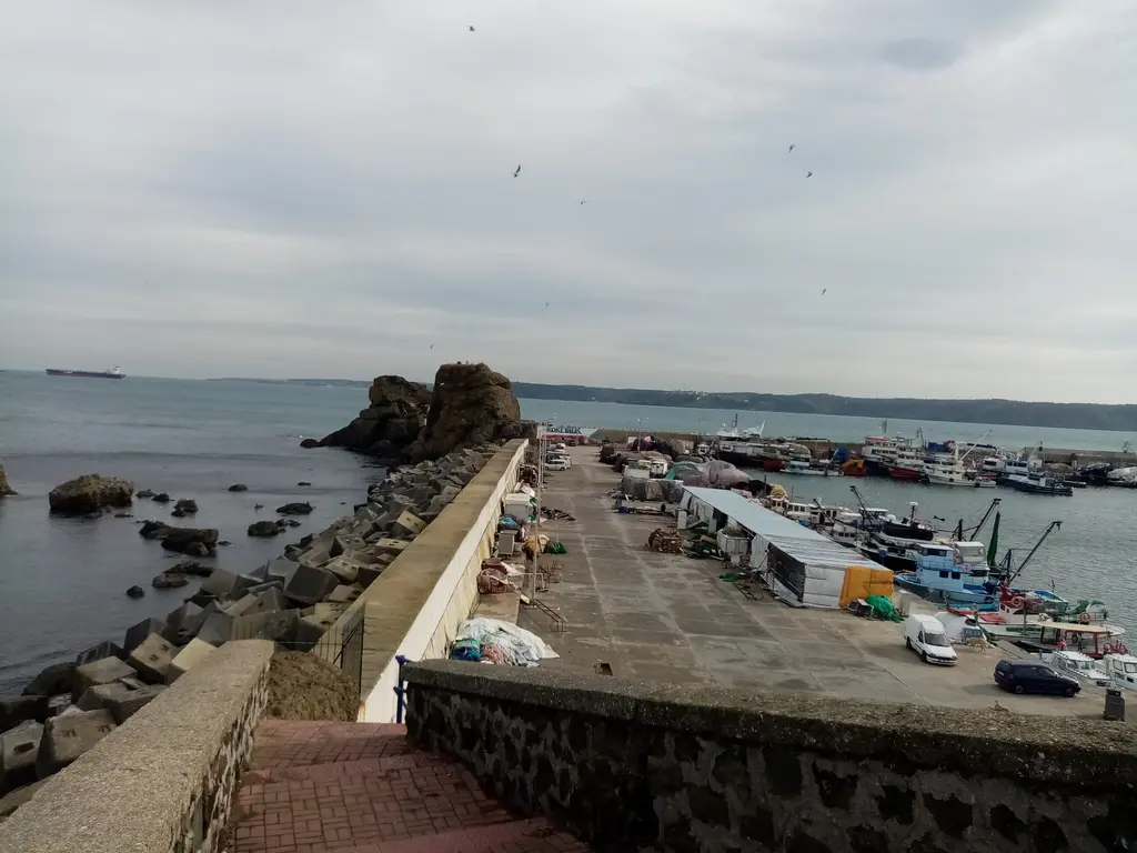 Rumelifeneri'nde dalgakıran; denize uzanan beton yol, ucunda büyük kaya, solda balıkçı limanı ve tekneler.