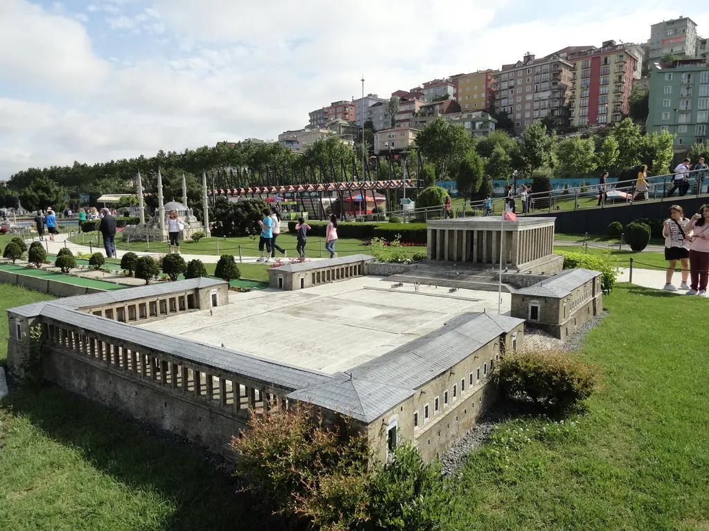 Miniatürk'te Anıtkabir maketi; sütunlu tören meydanı ve mozole, çimen üzerinde, arkada yürüyen gençler, ağaçlar ve renkli evler.