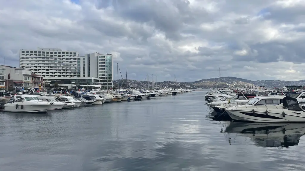 Tarabya Marinası; sakin suda demirli motorlu tekneler, rıhtım, kıyıdaki binalar ve uzakta otel yapısı.