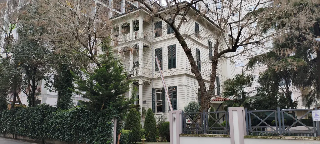 Göztepe'de Avcı Sokak'ta köşk; beyaz ahşap cepheli üç katlı yapı, kemerli balkonlar, çıplak ağaçlar ve demir kapı.