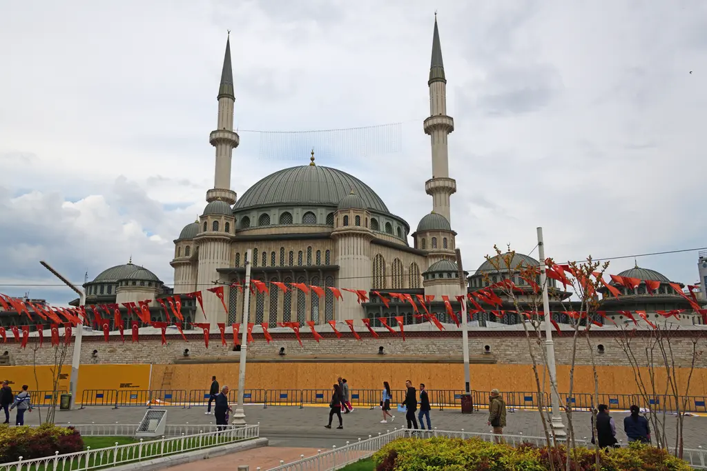 Taksim Meydanı'ndan Taksim Camii; geniş taş meydan, önde çit ve yeşil alan, arkada kubbeler ve iki minare.