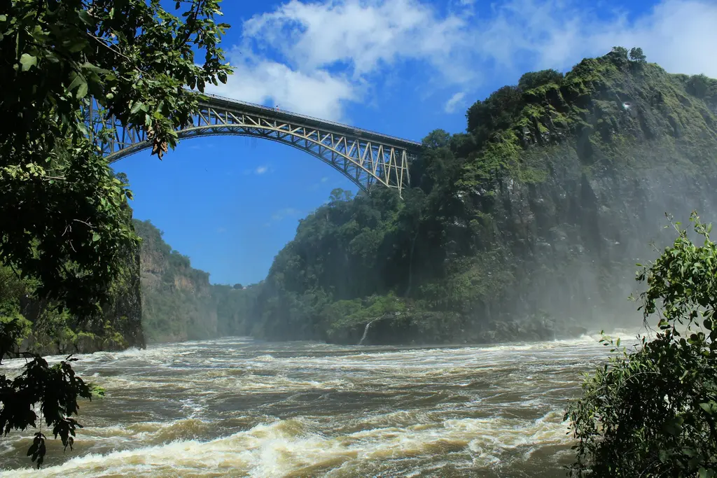 Zimbabve'de Victoria Şelalesi kanyonu; derin geçidin üzerinde çelik kemerli köprü, altında köpüklü Zambezi Nehri ve şelalenin sisi.
