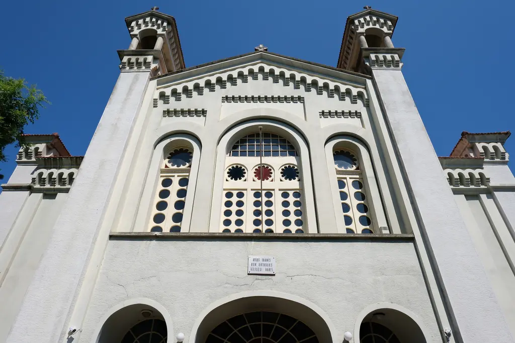 Burgazada'da Ayios Ioannes Prodromos Kilisesi; taş ve sıva cephe, çan kulesi ve önünde ağaçlar.
