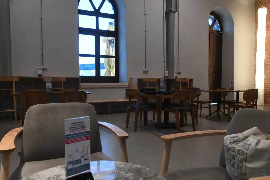 Feshane'de kafe; kemerli büyük pencereler, ahşap uzun masa, sandalyeler, demir sütun ve içeri dolan gün ışığı.