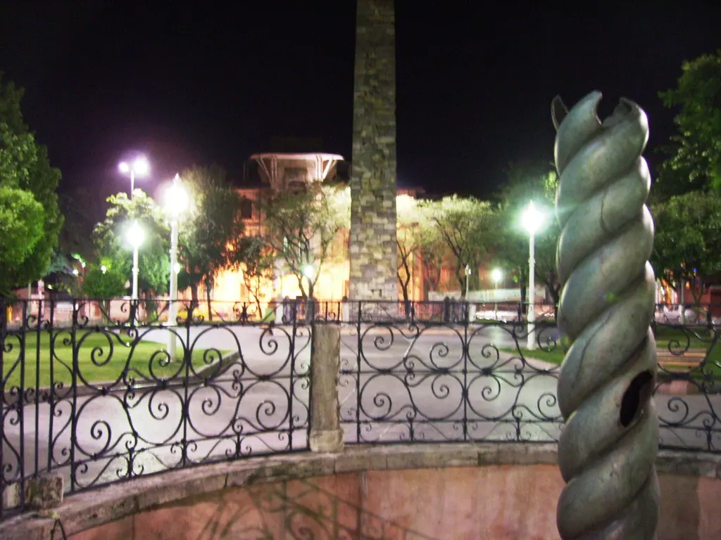 Gece Sultanahmet Meydanı; önde Yılanlı Sütun'un burmalı gövdesi, arkada aydınlatılmış Dikilitaş, palmiyeler ve sokak lambaları.