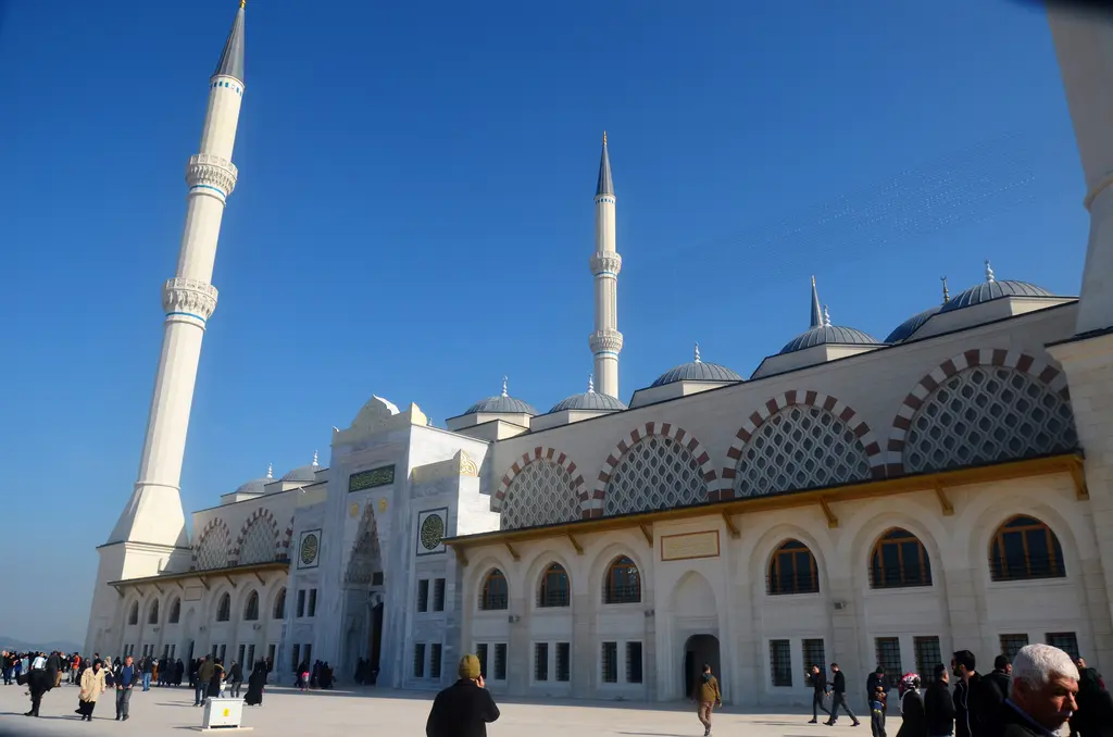 Büyük Çamlıca Camii'nin yan cephesi; kemerli pencere sıraları, kubbeler, minare ve önünde yürüyenler.