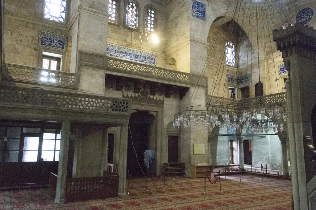 Sokullu Mehmed Paşa Camii'nde harim ve mahfil; kemerli galeri, ahşap korkuluk, aşağıda halı kaplı zemin ve üstte avizeler.