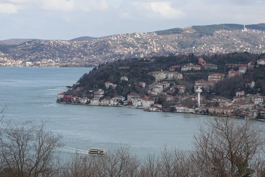 Kanlıca'dan Boğaz; kıyıya dizilen yalılar, ağaçlık burun, beyaz kule ve arkada yamaçlara yayılan şehir.
