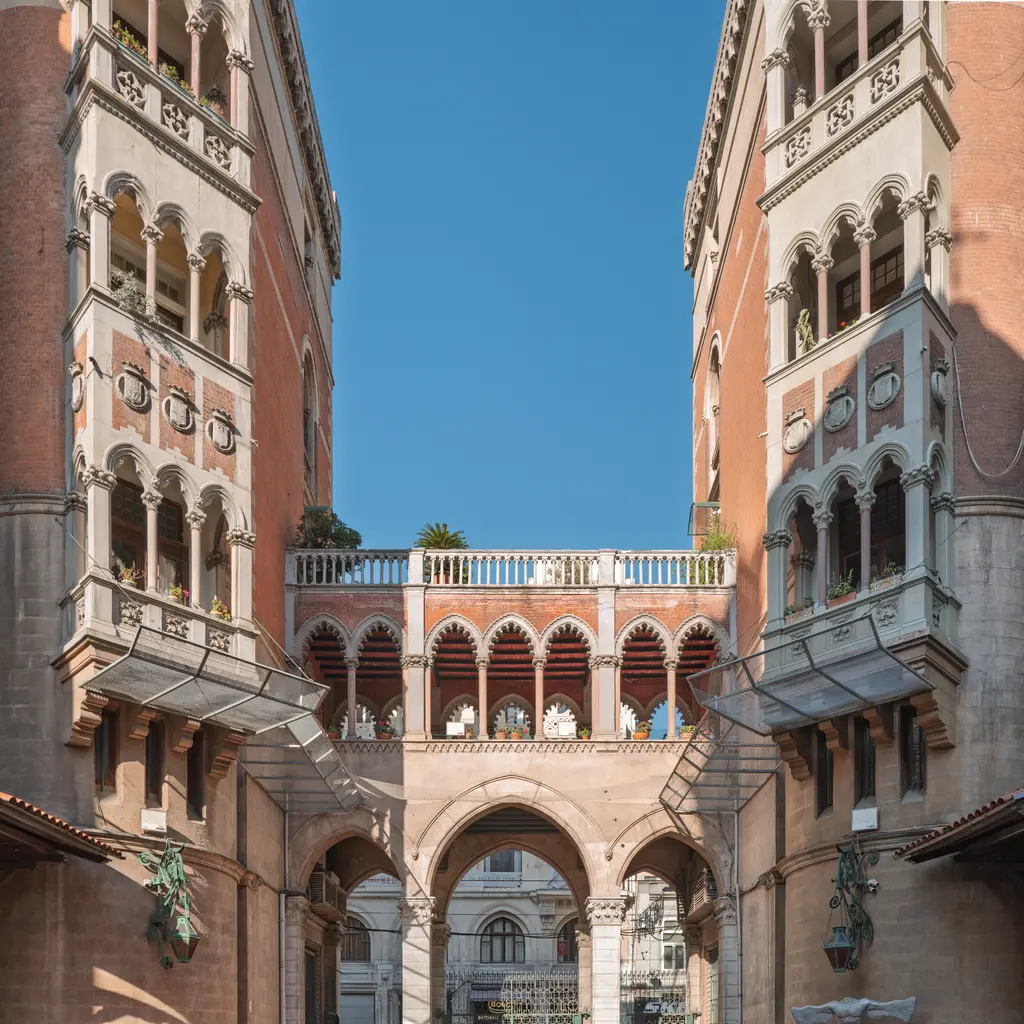 Sent Antuan avlusunun İstiklal tarafı; iki yanda kule biçimli apartman köşeleri, ortada kemerli galerili geçit ve mavi gökyüzü.