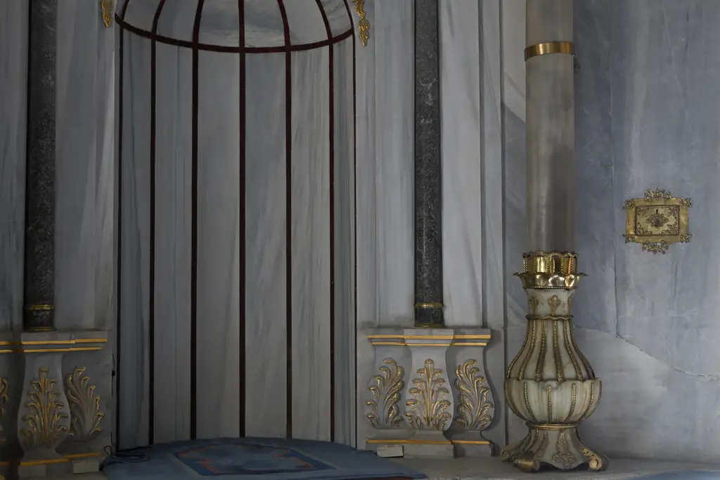 Nusretiye Camii'nde mihrap tarafından ayrıntı; beyaz mermer yüzeyler, yaldızlı sütun başlıkları ve büyük yaldızlı şamdan.