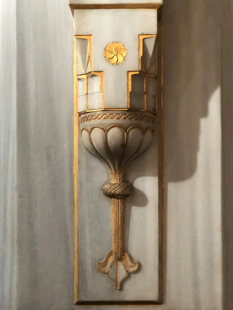Şişli Camii'nde mermer duvara oturan aplik; yaldızlı çerçeve, kandil biçimli kâse ve altında sarkan süs.