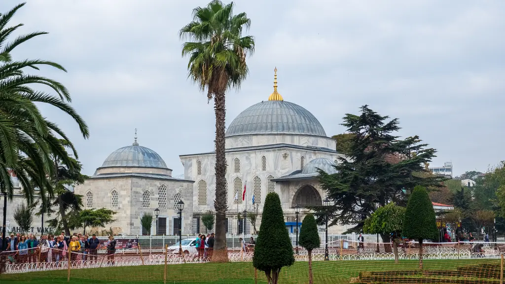 Sultanahmet Meydanı'ndan türbe ve darülkurrâ; solda küçük kubbeli yapı, sağda büyük kubbeli türbe, önde palmiye, sedir ve budanmış ağaçlar.