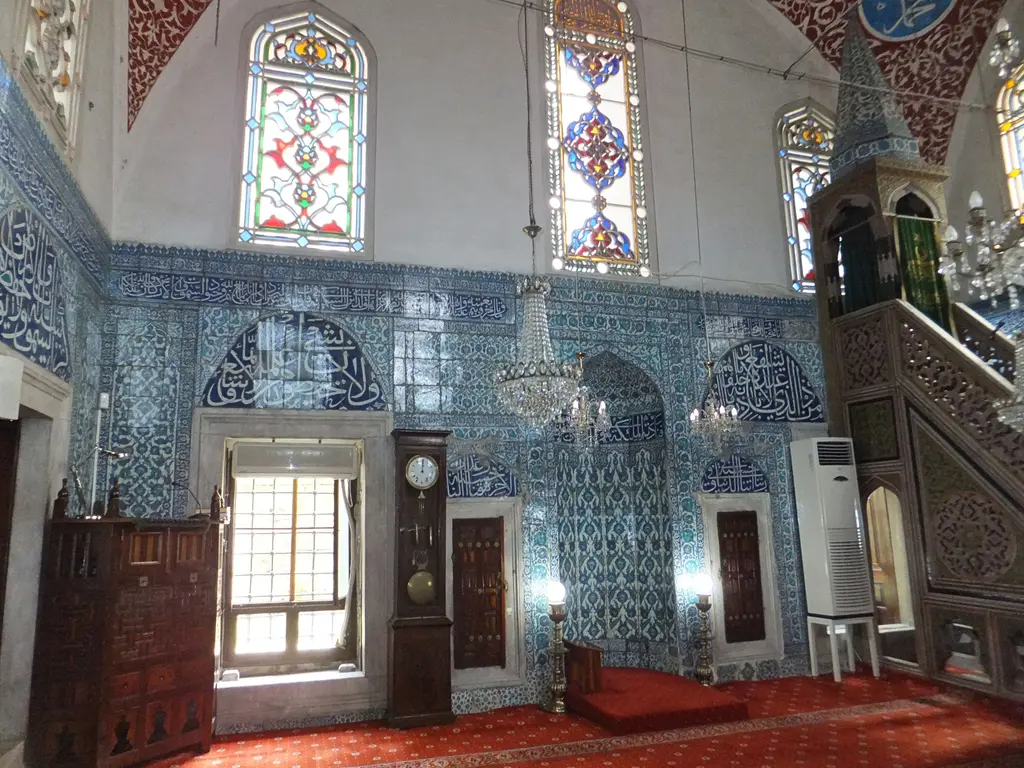 Çinili Camii'nin içi; mavi çinili duvarlar, renkli vitray pencereler, ahşap dolaplar, saat ve çinili minber.