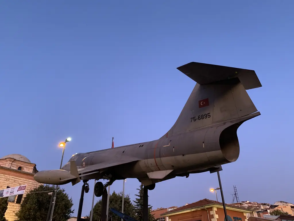 Rahmi Mustafa Koç Müzesi'nde F-104 Starfighter; mavi gökyüzüne karşı direk üzerinde duran gri jet avcısı, T biçimli kuyruk ve arkada bir bina.