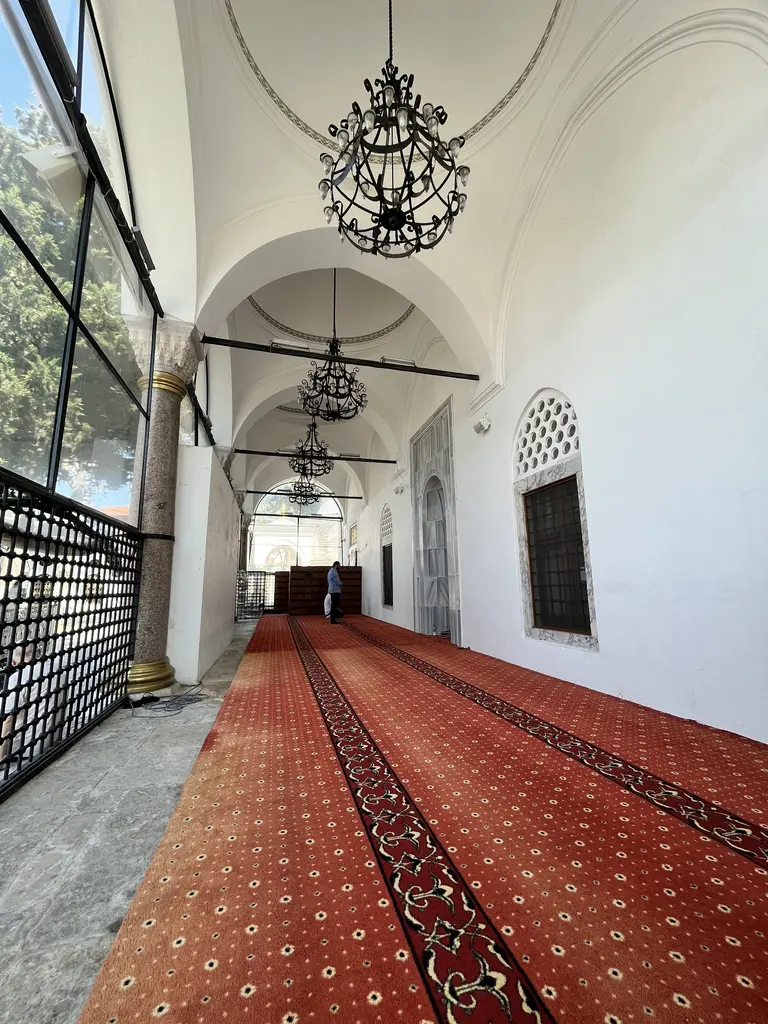 Koca Mustafa Paşa Camii'nin camekânla kapatılmış son cemaat yeri; solda boydan boya cam, sağda beyaz badanalı duvar ile sivri kemerli pencere, tavanda tonozlar ve dövme demir avizeler.