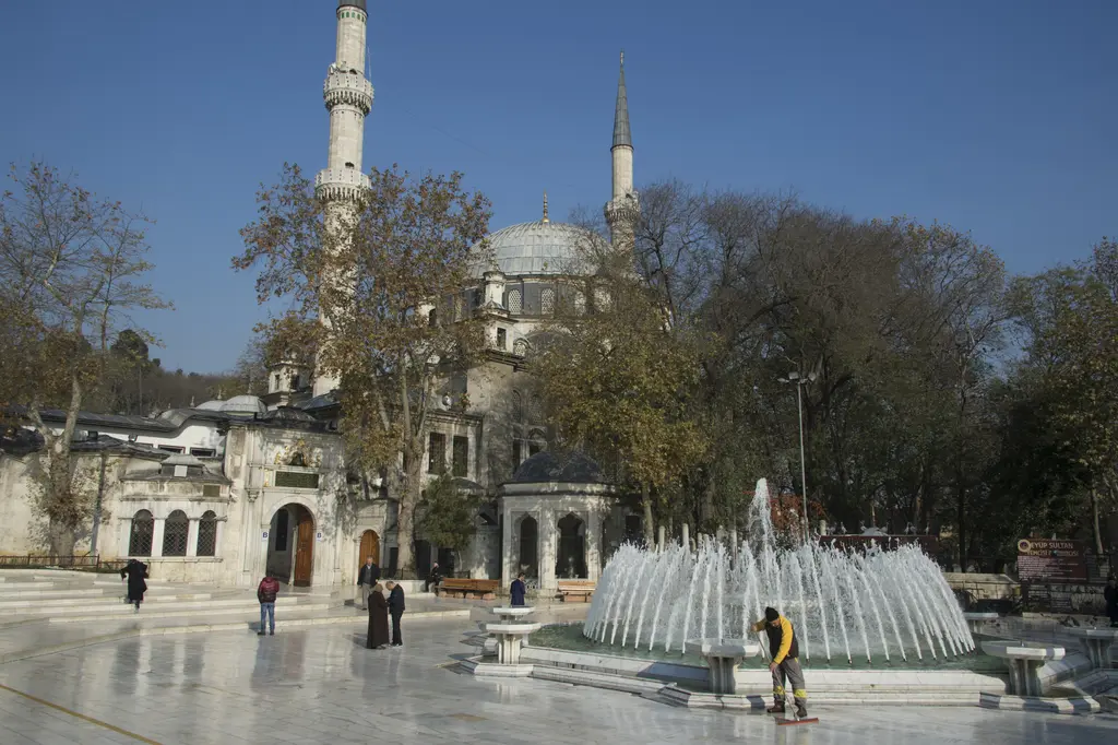 Eyüpsultan'da Eyüp Sultan Camii; iki ince minare, kurşun kubbe, ağaçlar ve önündeki meydanda fıskiyeli havuz.