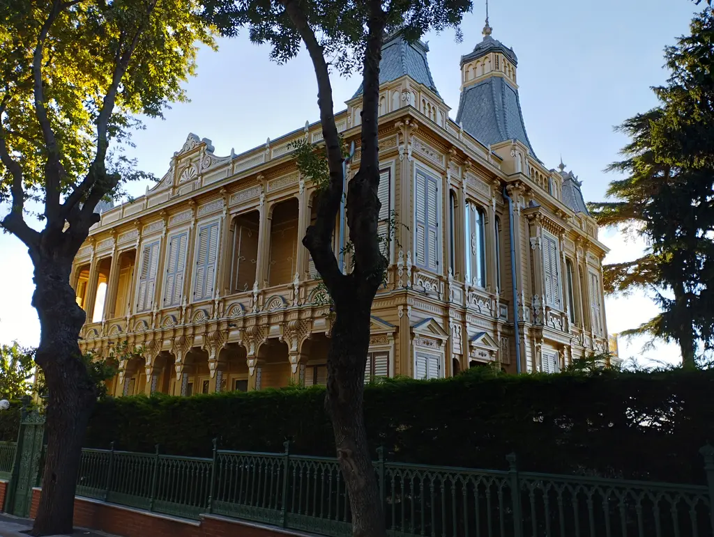 Büyükada'da köşk; sarı cepheli, kuleli büyük konak, demir parmaklıklı bahçe ve önünde yaşlı ağaçlar.