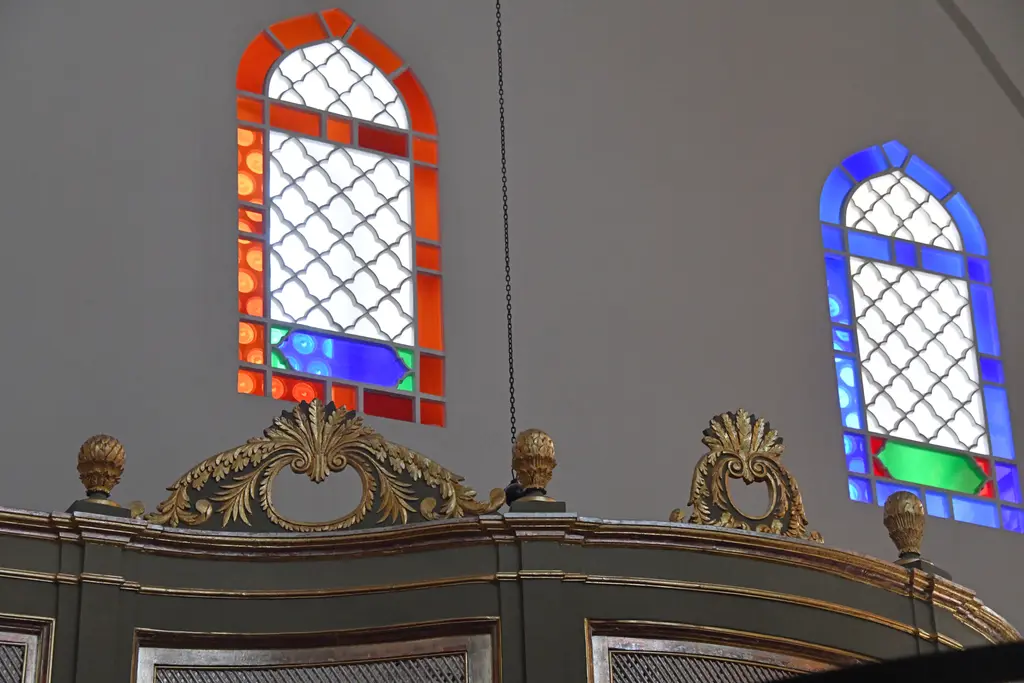 Mahmut Paşa Camii'nde hünkâr mahfilinin tepesi; yaldızlı kıvrımlı süslemeler, gri ahşap panolar ve arkada kırmızı ile mavi camlı pencereler.