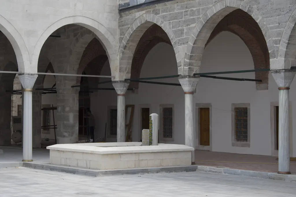 Mihrimah Sultan Camii avlusunun güneydoğu köşesinde mermer mezar; alçak sanduka, çevresindeki taş döşeme ve arkada revak kemerleri.