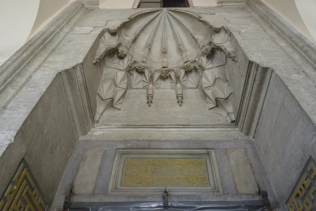 Haseki Sultan Camii'nin taç kapısı; mukarnaslı kavsara, altında sarı zeminli yazı levhası ve iki yanda köşeli kufi yazı panoları.