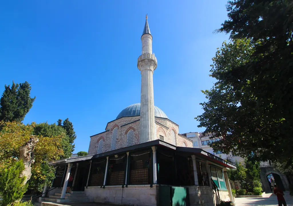 Üsküdar'da Çinili Camii; kurşun kubbe, ince tek minare, önde ahşap çatılı son cemaat yeri ve çevresinde ağaçlar.