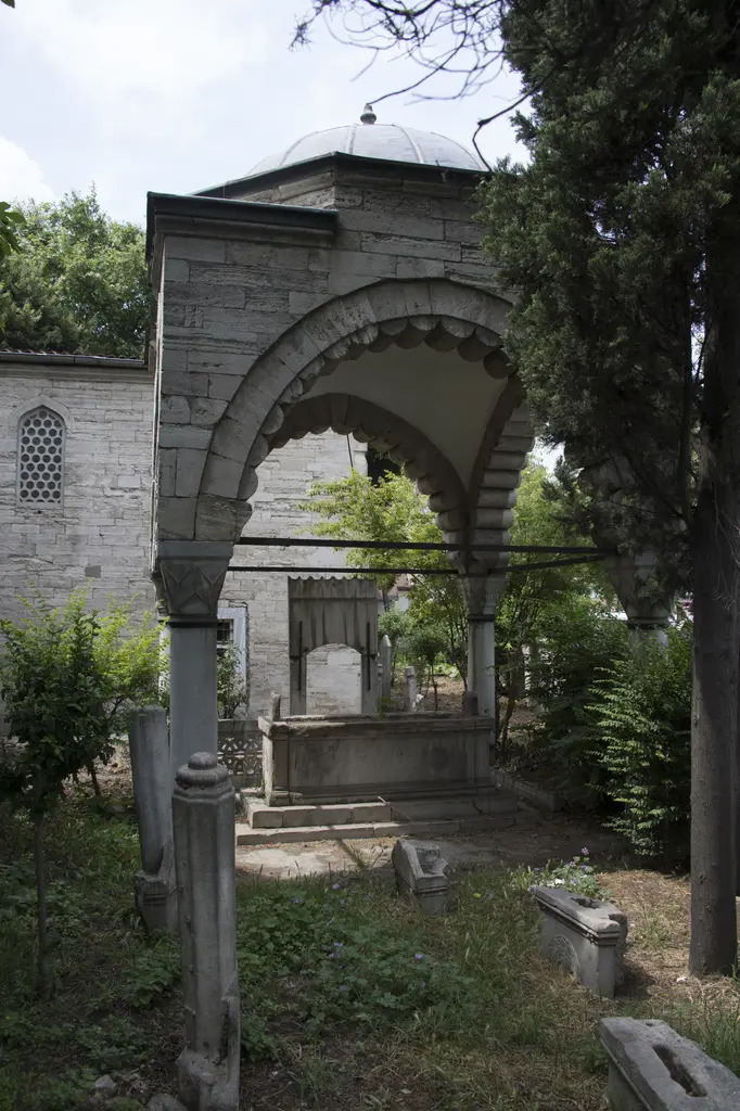 Defterdar Mahmud Çelebi Türbesi; yarım yuvarlak dilimli taş kemerler, köşe sütunları, sanduka ve önde eski mezar taşları.