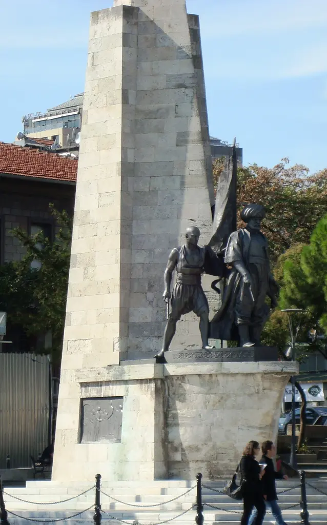Barbaros Anıtı; taş kaide ve bronz figürler, önünden geçen yayalar ve arkada Beşiktaş'ın binaları.